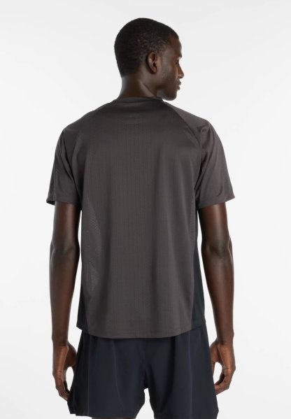 Hombre que lleva una camiseta de manga corta gris oscuro y pantalones cortos negros, de pie de espaldas sobre un fondo blanco.