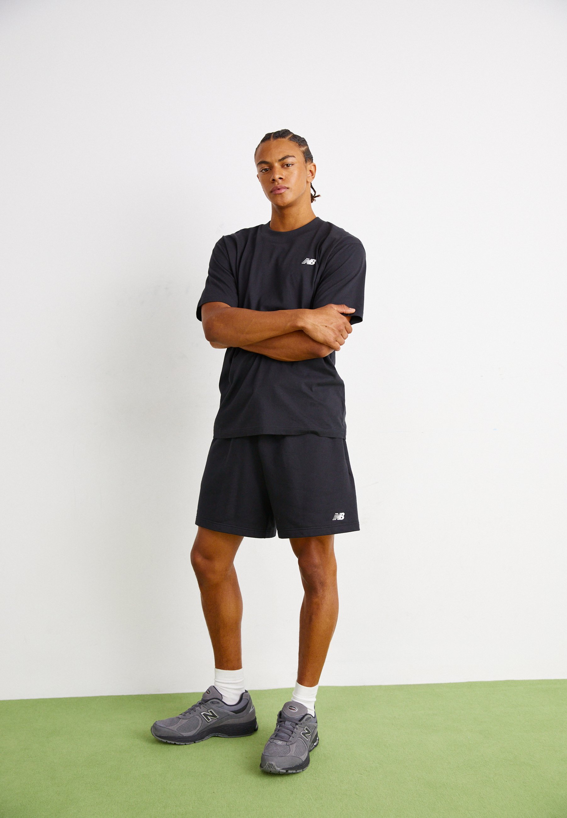 Conjunto de camiseta de algodón negro y pantalones cortos con un pequeño logo blanco en el pecho; combinado con zapatillas deportivas grises y calcetines blancos hasta el tobillo.