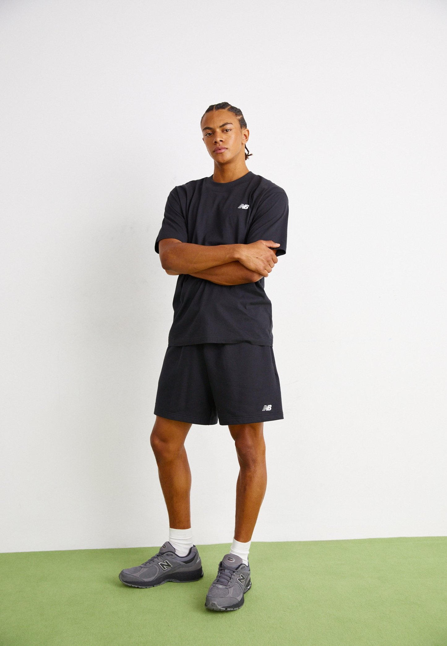Conjunto de camiseta de algodón negro y pantalones cortos con un pequeño logo blanco en el pecho; combinado con zapatillas deportivas grises y calcetines blancos hasta el tobillo.