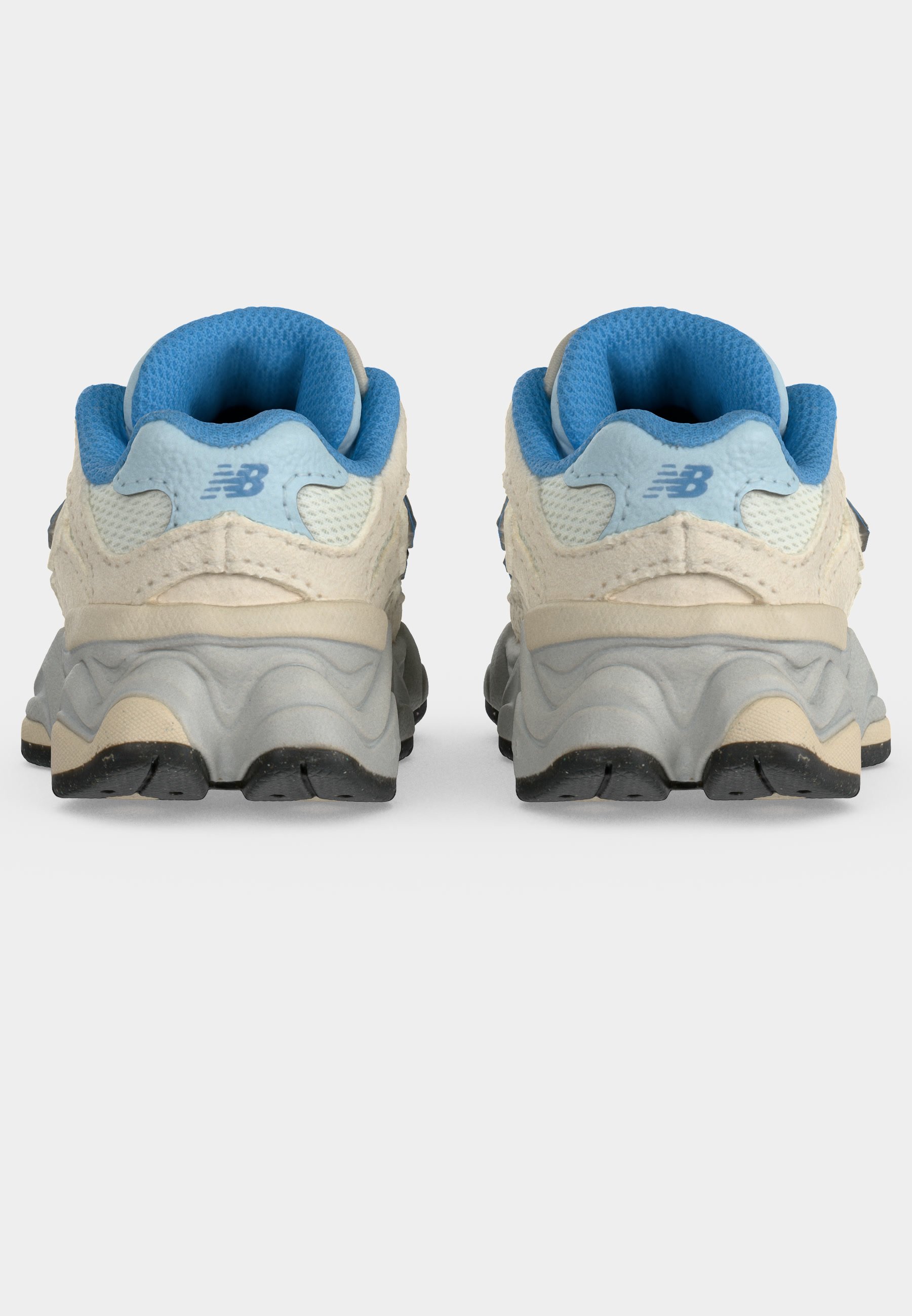 Par de zapatillas deportivas blancas y azul claro vistas desde atrás, mostrando interiores acolchados azules y suelas gruesas texturizadas de color gris.
