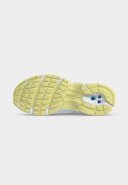 Suela de una zapatilla de running New Balance amarilla con agarre texturizado y amortiguación azul visible en el área del talón sobre un fondo blanco liso.