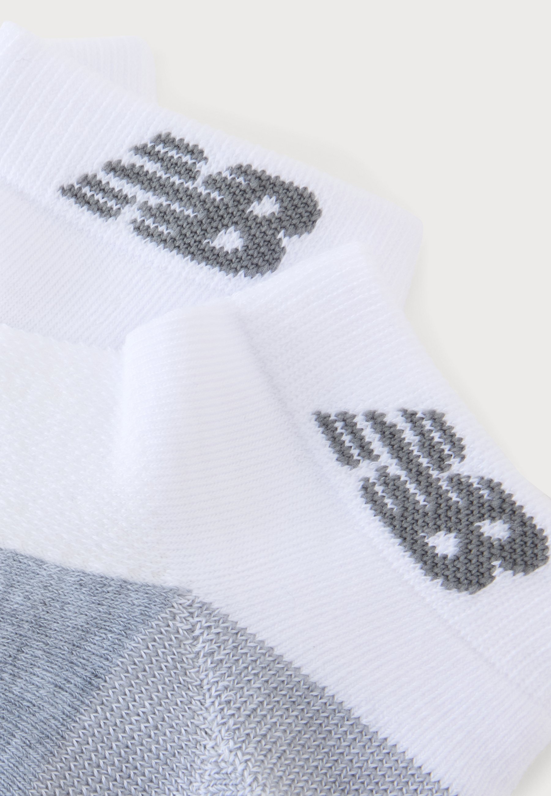 Calcetines tobilleros blancos y grises con un logo gris oscuro tejido cerca del puño sobre un fondo claro y liso.