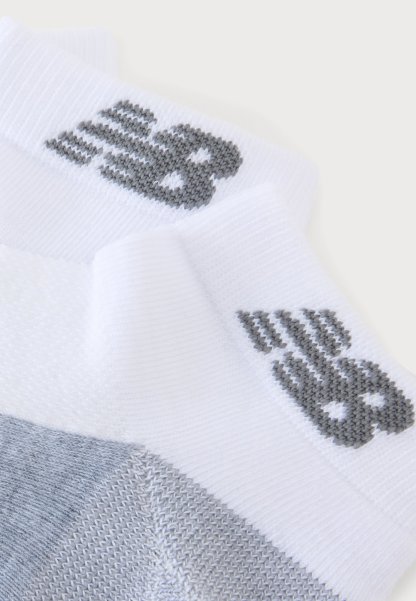 Calcetines tobilleros blancos y grises con un logo gris oscuro tejido cerca del puño sobre un fondo claro y liso.