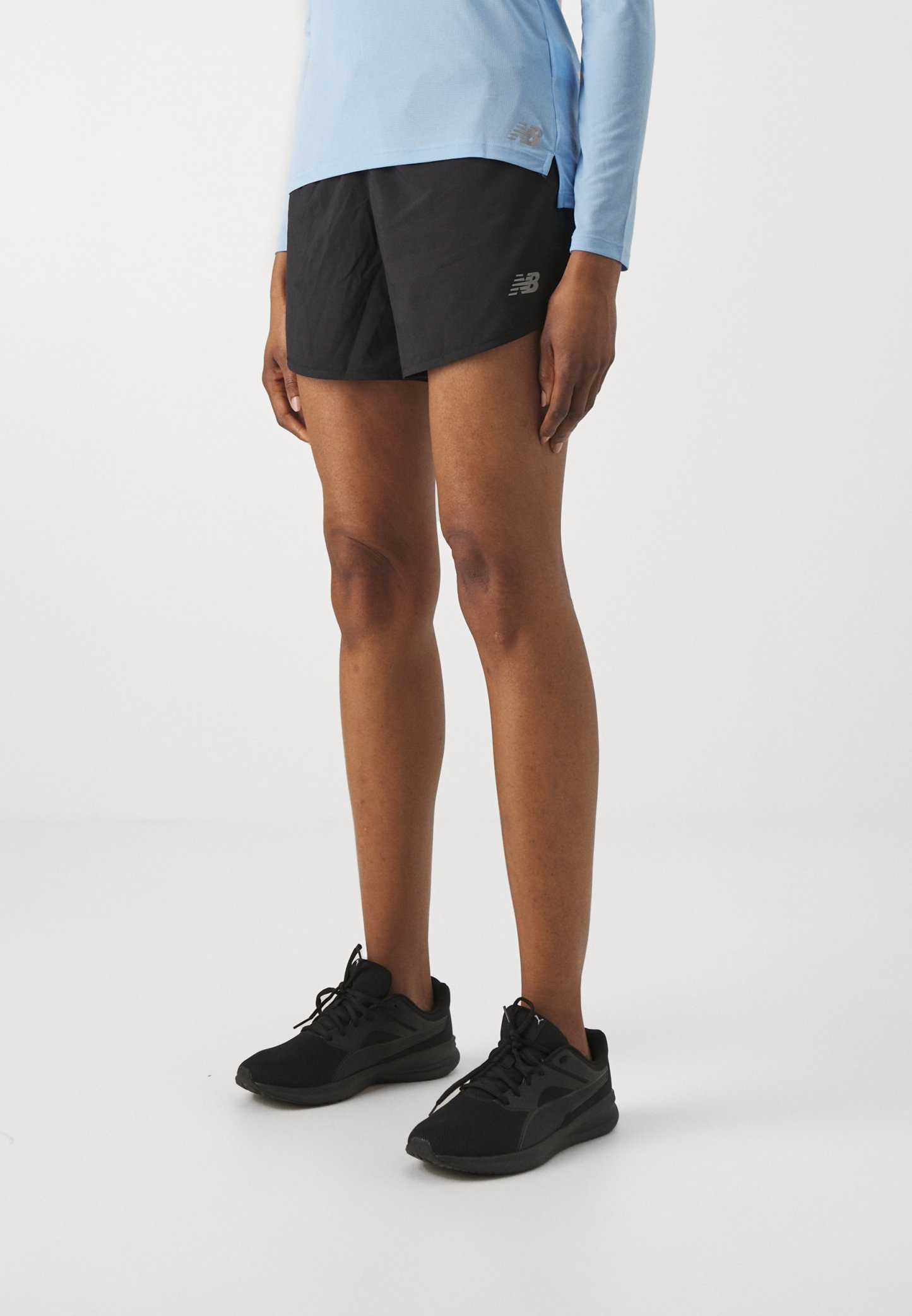 Los pantalones cortos deportivos negros cuentan con una tela ligera y texturizada. Combinados con zapatillas de correr negras, ideales para el uso activo. Top de manga larga de color azul claro.