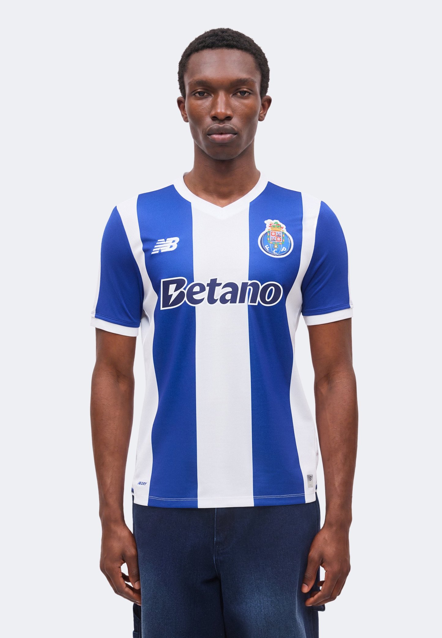 Hombre con camiseta de fútbol del FC Porto a rayas verticales azules y blancas con el logo del patrocinador Betano, posando frente a un fondo claro liso.
