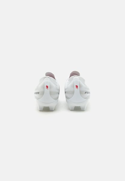 Botas de fútbol blancas con tejido texturizado y logotipos rojos de New Balance, mostradas desde atrás sobre un fondo liso.