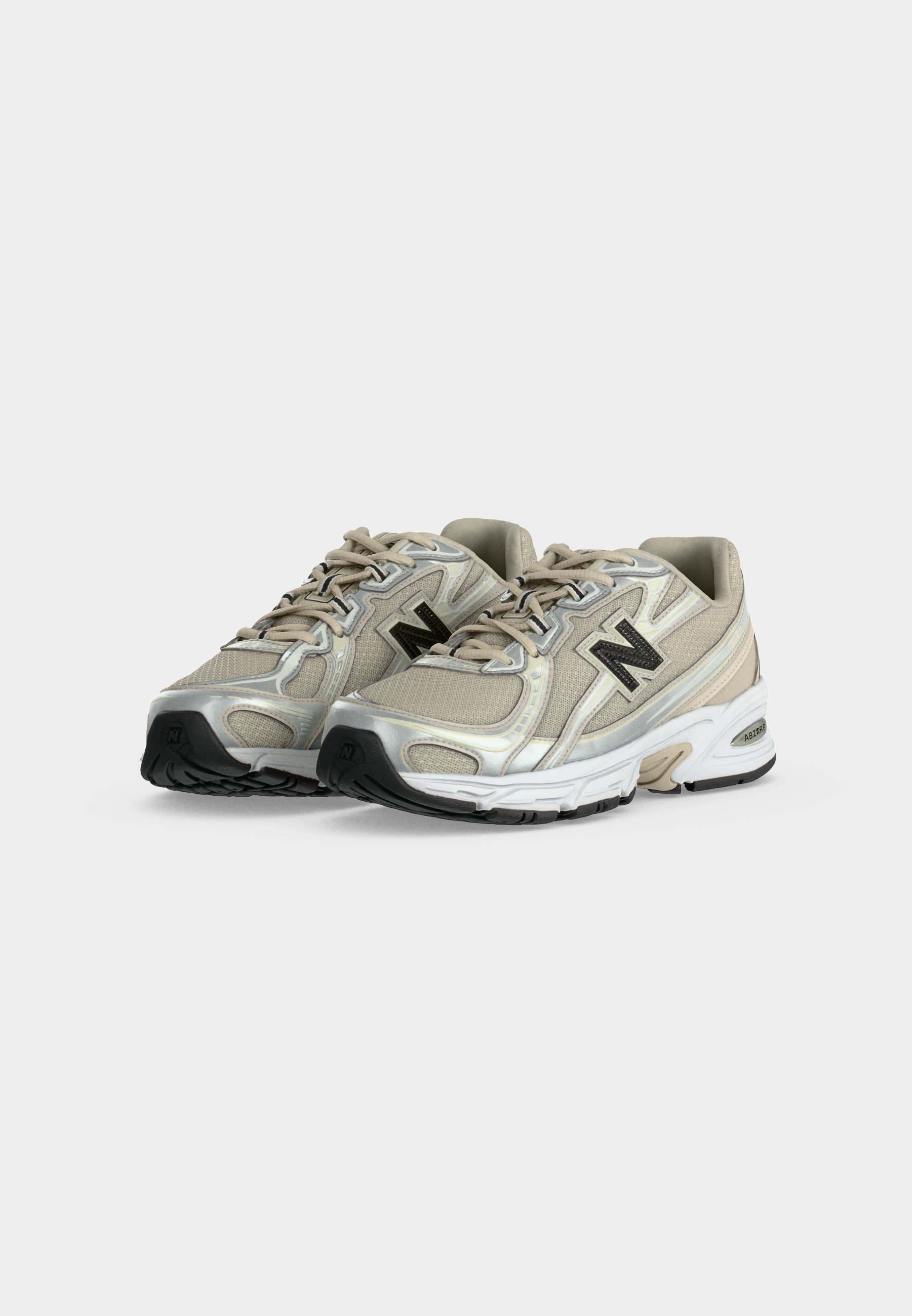 Par de zapatillas de running New Balance beige y plateadas con suelas negras y logo, mostradas lado a lado sobre un fondo liso.