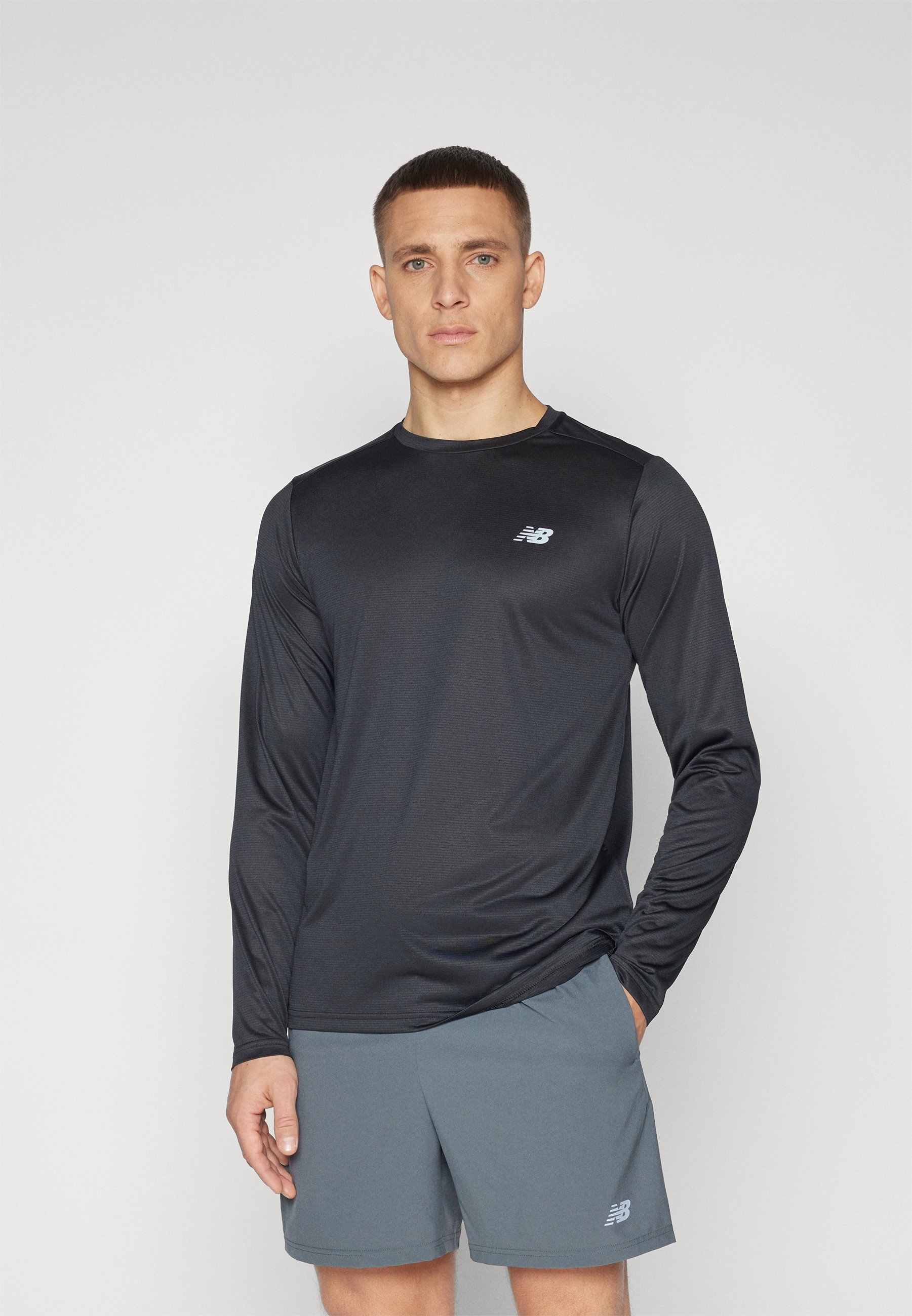Camiseta atlética negra de manga larga en tejido suave con una sutil textura, que presenta un pequeño logo gris en el pecho. Lleva puestos unos pantalones cortos grises.