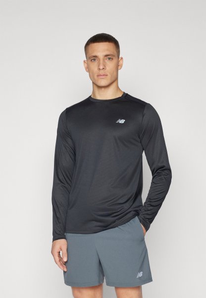 Camiseta atlética negra de manga larga en tejido suave con una sutil textura, que presenta un pequeño logo gris en el pecho. Lleva puestos unos pantalones cortos grises.