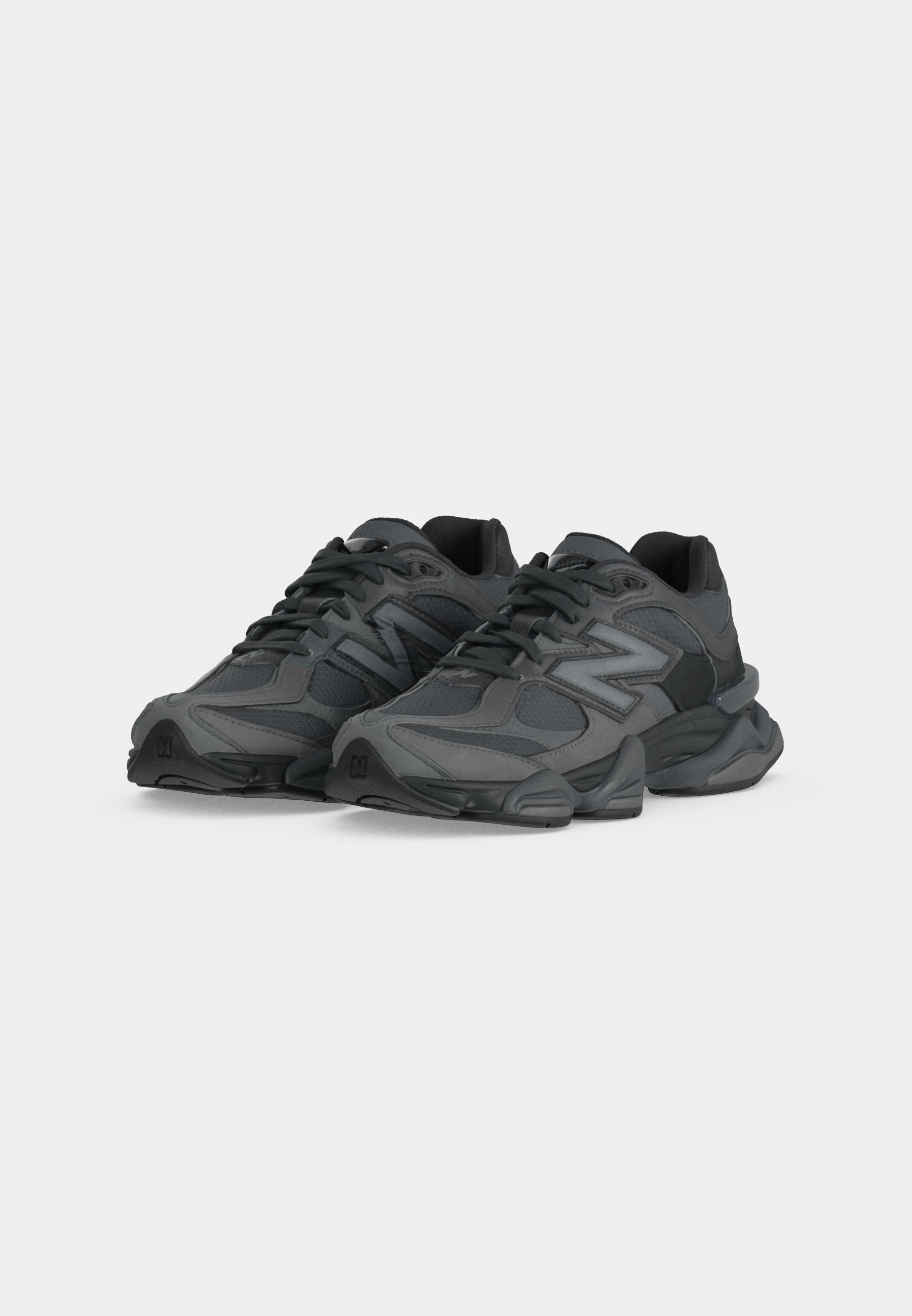Par de zapatillas deportivas negras y gris oscuro con suelas gruesas y diseño con cordones sobre un fondo claro y liso.