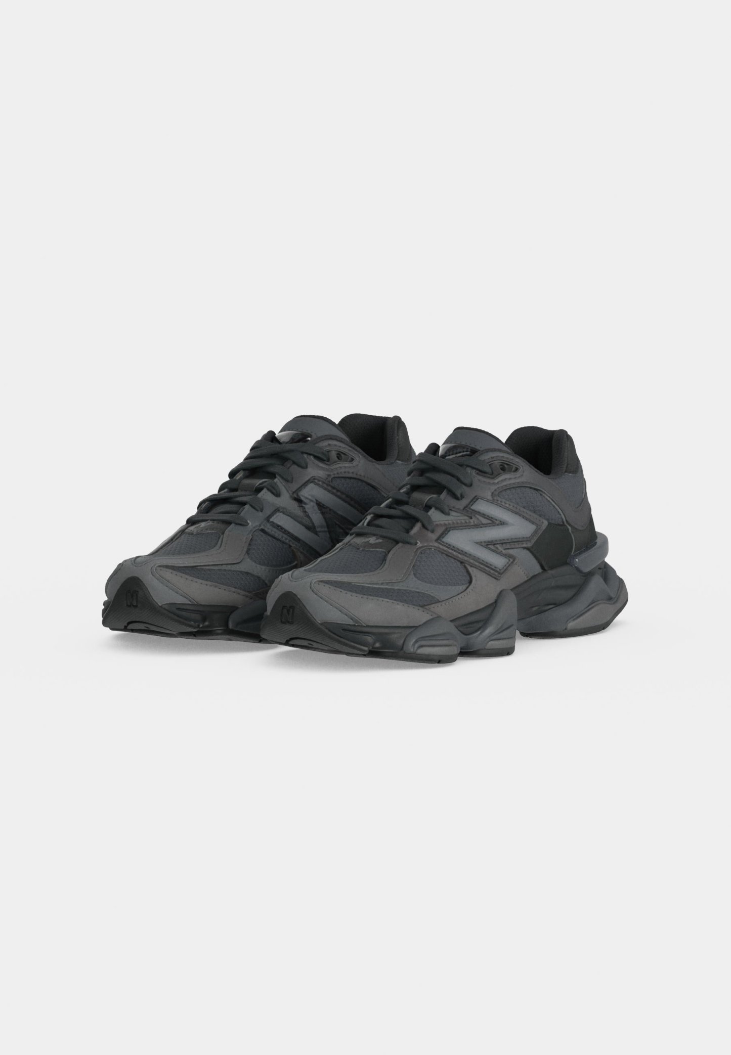Par de zapatillas deportivas negras y gris oscuro con suelas gruesas y diseño con cordones sobre un fondo claro y liso.