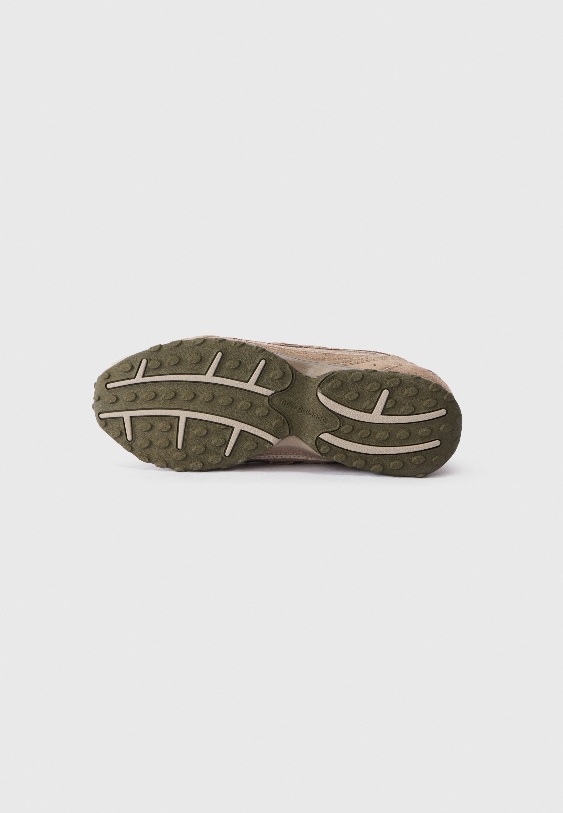 Suela de zapatilla marrón con banda de goma texturizada verde y surcos de color beige claro, exhibida sobre un fondo blanco sencillo.