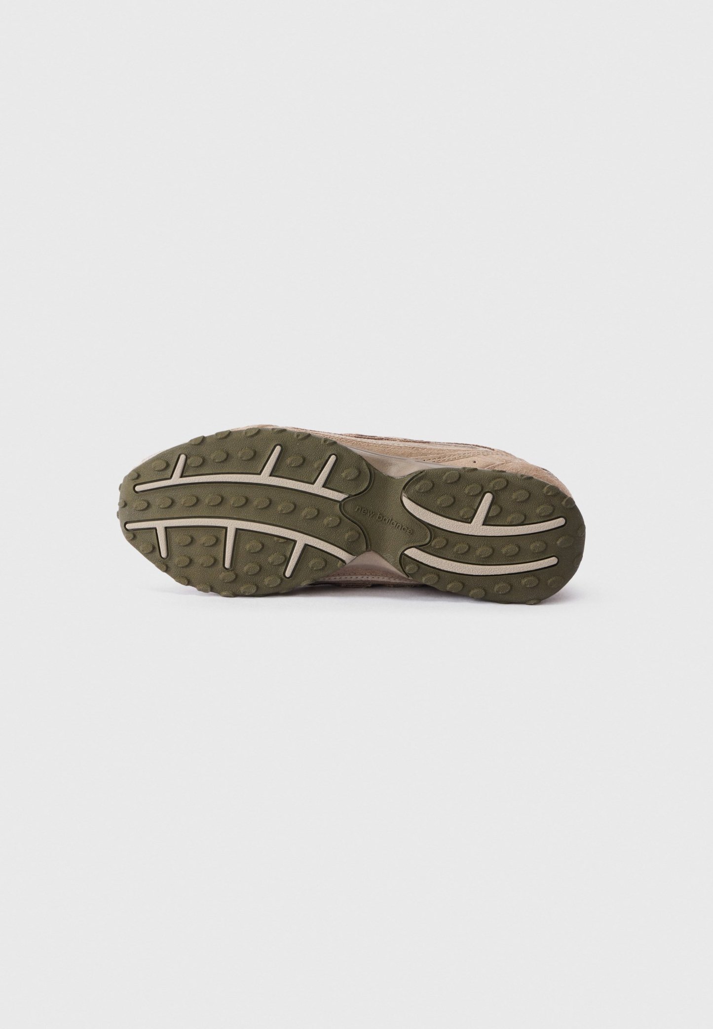 Suela de zapatilla marrón con banda de goma texturizada verde y surcos de color beige claro, exhibida sobre un fondo blanco sencillo.