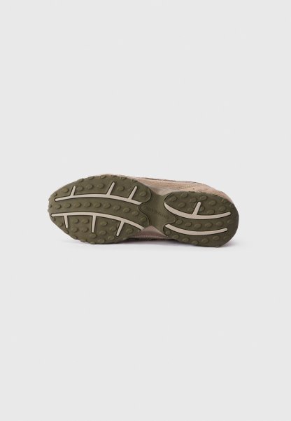 Suela de zapatilla marrón con banda de goma texturizada verde y surcos de color beige claro, exhibida sobre un fondo blanco sencillo.