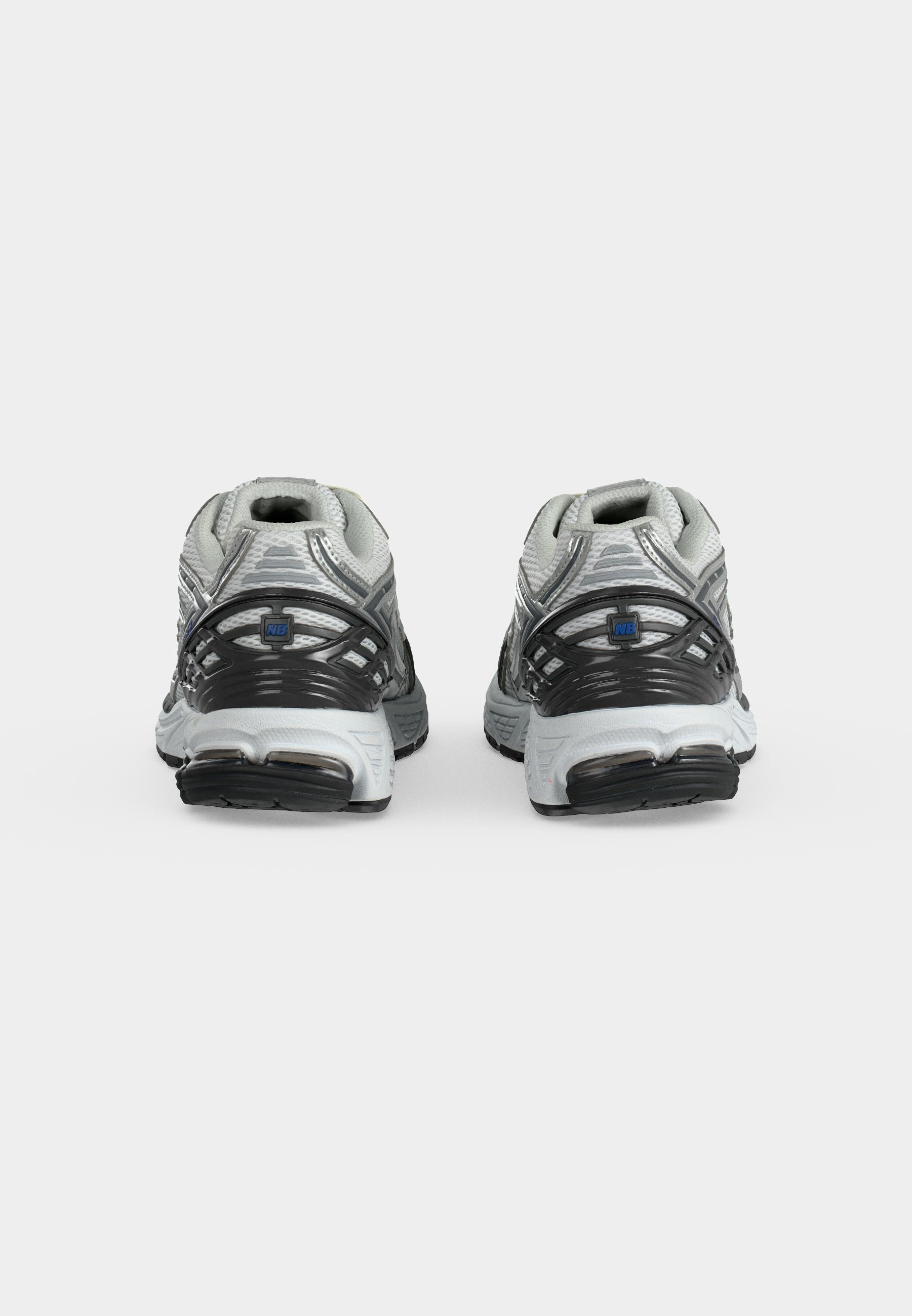 Par de zapatillas de running New Balance grises y blancas con suelas negras, parte superior de malla y cordones beige sobre un fondo blanco liso.