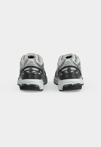 Par de zapatillas de running New Balance grises y blancas con suelas negras, parte superior de malla y cordones beige sobre un fondo blanco liso.