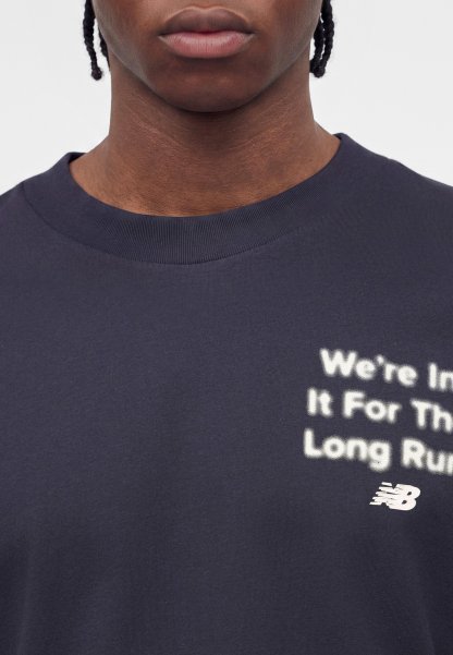 Primer plano de una persona que lleva una camisa azul marino oscura con texto blanco parcialmente visible que dice "We're In It For The Long Run" y un logotipo de New Balance.
