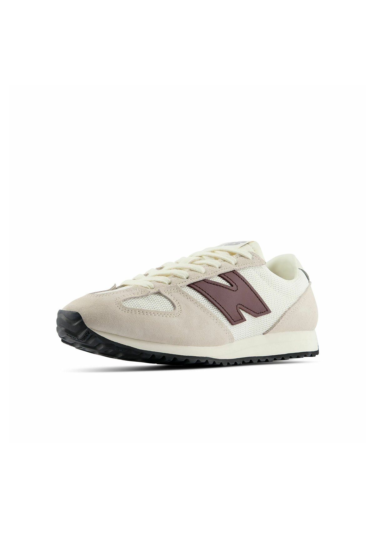 Zapatilla beige y blanca con logo lateral marrón, cordones frontales y suela negra texturizada, mostrada en un ligero ángulo sobre un fondo blanco.