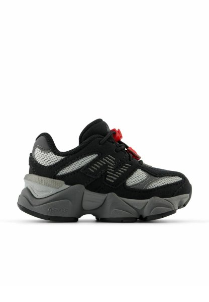 Zapatilla deportiva en negro y gris con parte superior de malla, suela de goma gruesa, acentos rojos y detalles geométricos en los laterales.