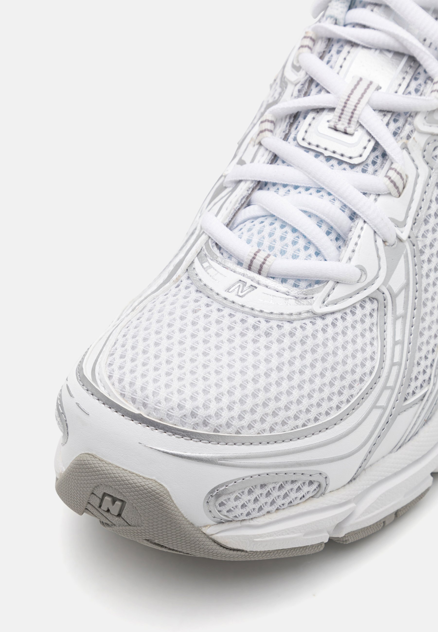 Zapatilla deportiva blanca con parte superior de malla, detalles texturizados, suela acolchada y acentos reflectantes. Cuentan con cordones y logotipo.