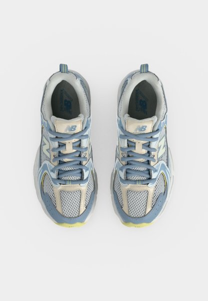 Par de zapatillas de running New Balance azules, grises y blancas vistas desde arriba, con detalles de malla y cuero y cordones azules.