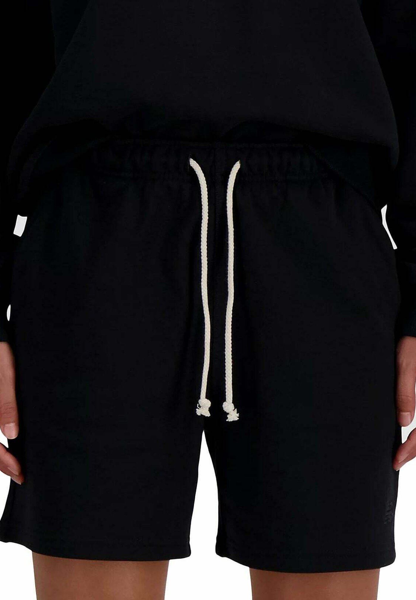 Persona vistiendo pantalones cortos negros con cordones largos y blancos, combinados con una camiseta negra, con las manos descansando a los lados.