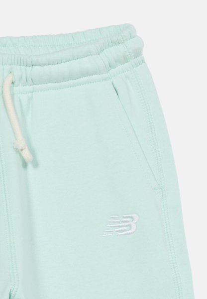 Pantalones deportivos azul claro con cintura elástica, cordón blanco, bolsillo lateral y logo bordado de New Balance en blanco justo debajo del bolsillo.