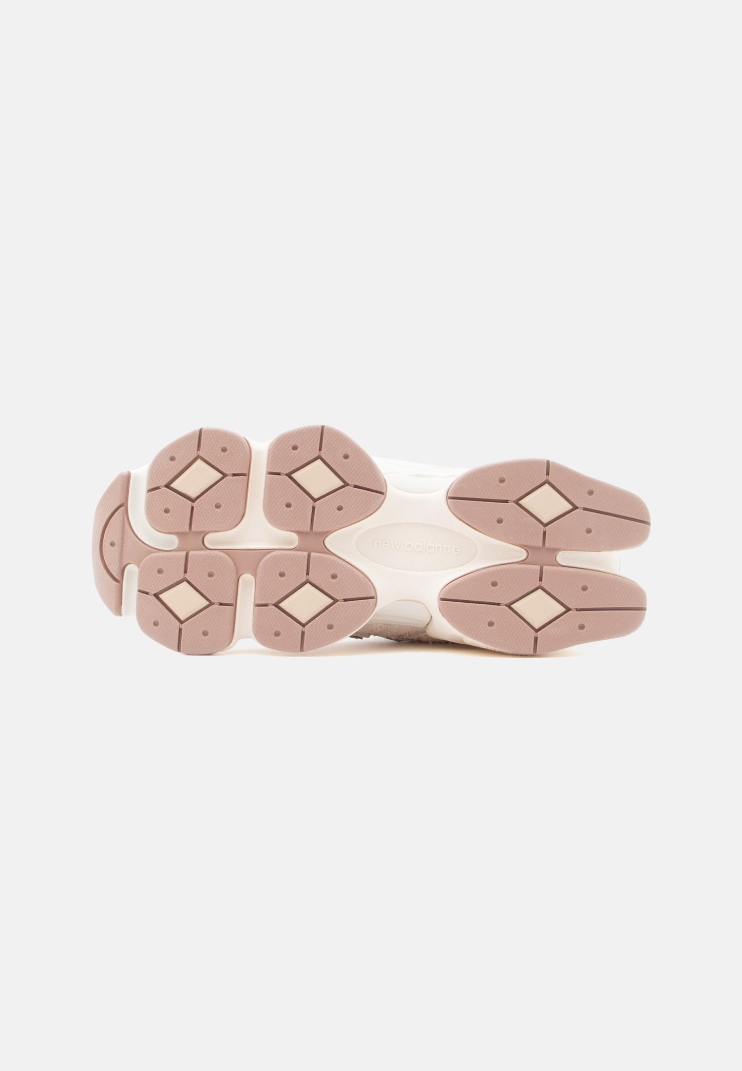 Suela de zapatilla New Balance beige y marrón claro con tacos en forma de diamante y agarre texturizado sobre fondo blanco.
