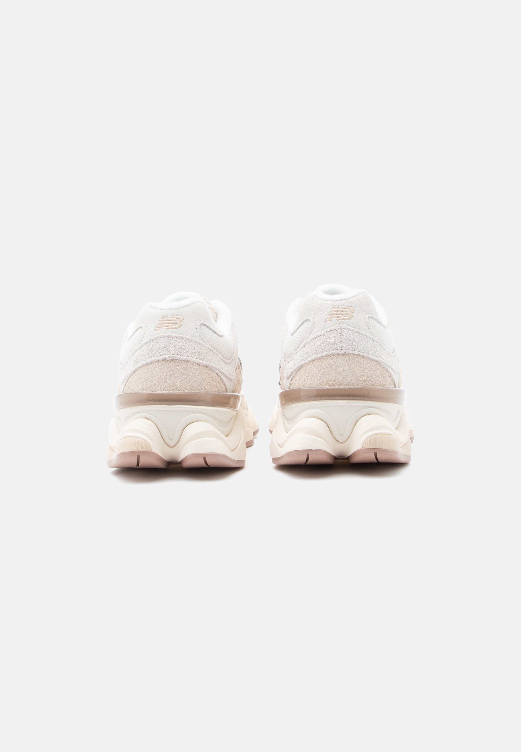 Zapatillas New Balance en blanco y beige vistas desde atrás, con suelas gruesas y ante texturizado, sobre un fondo liso gris claro.