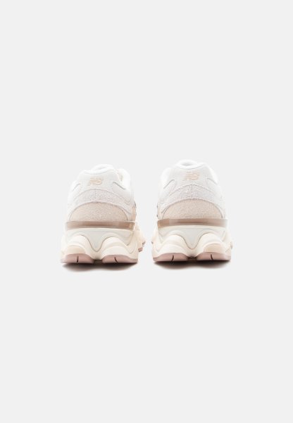 Zapatillas New Balance en blanco y beige vistas desde atrás, con suelas gruesas y ante texturizado, sobre un fondo liso gris claro.