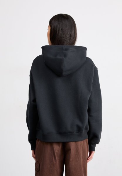 Sudadera con capucha negra de gran tamaño, con una textura suave, puños y dobladillo acanalados. Llevada sobre pantalones cargo marrones, vista desde la parte posterior.