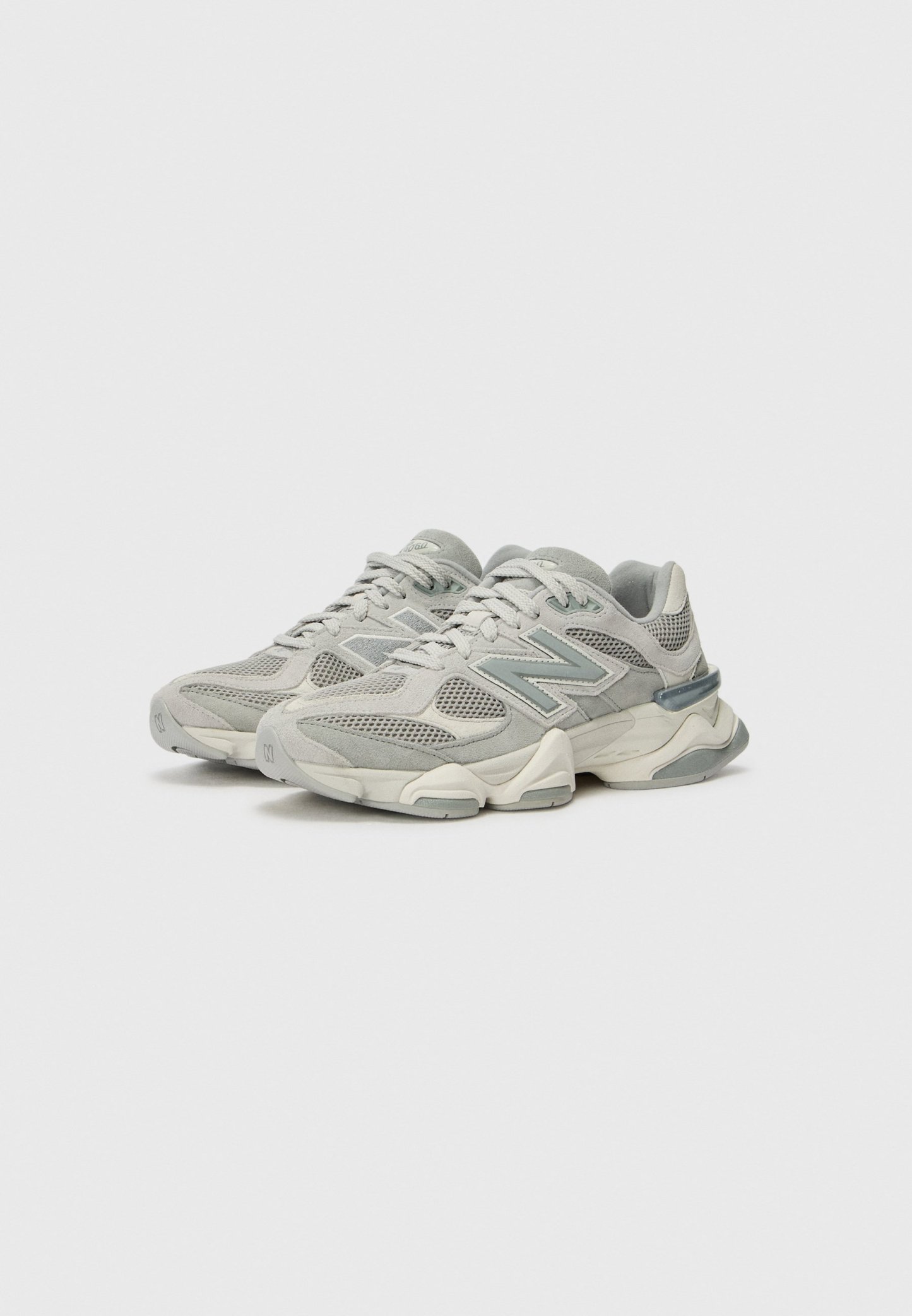 Par de zapatillas New Balance en gris y blanco roto con paneles de malla y ante, suela gruesa y cierre de cordones, mostradas una al lado de la otra.