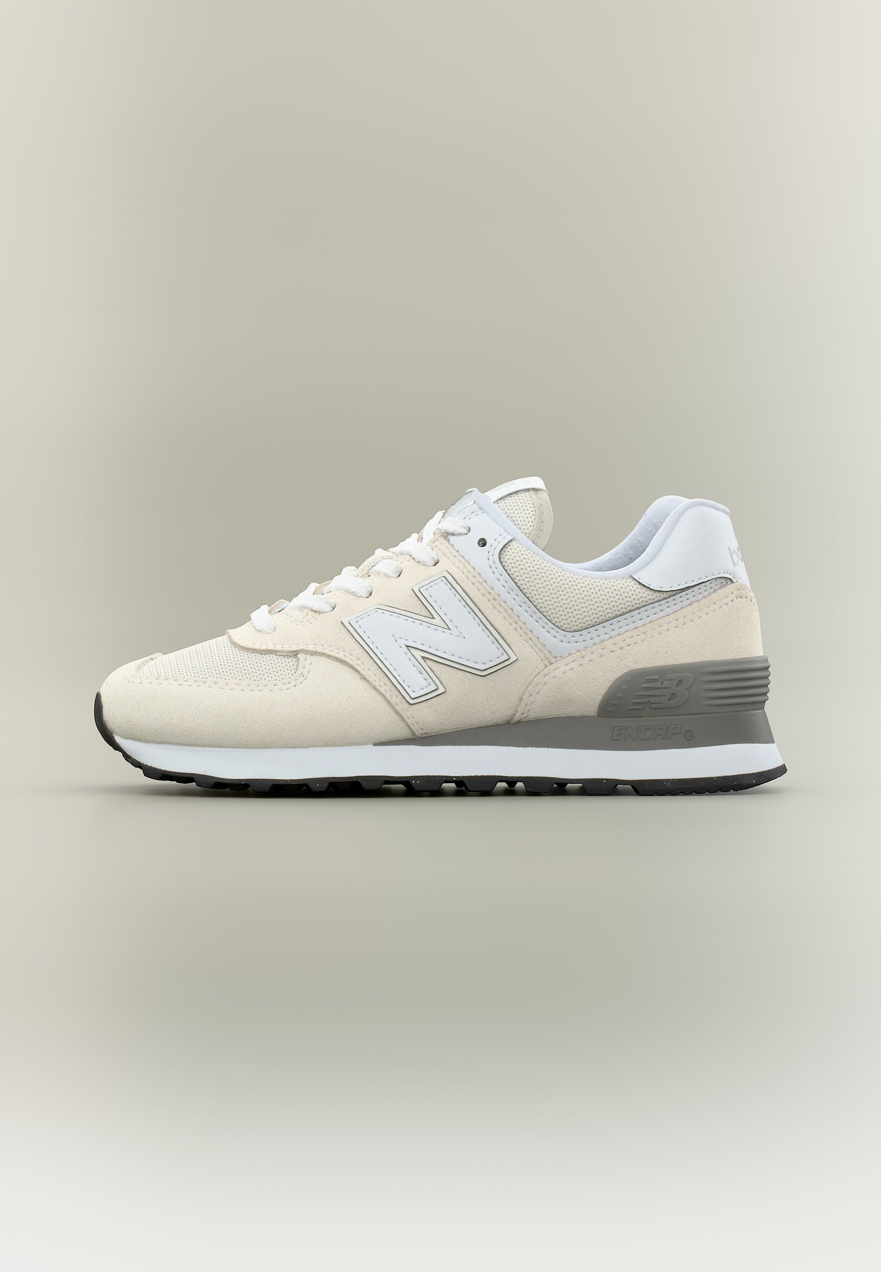 Zapatilla New Balance beige y blanca con parte superior de malla y ante, diseño con cordones y suela acolchada gris sobre fondo beige.