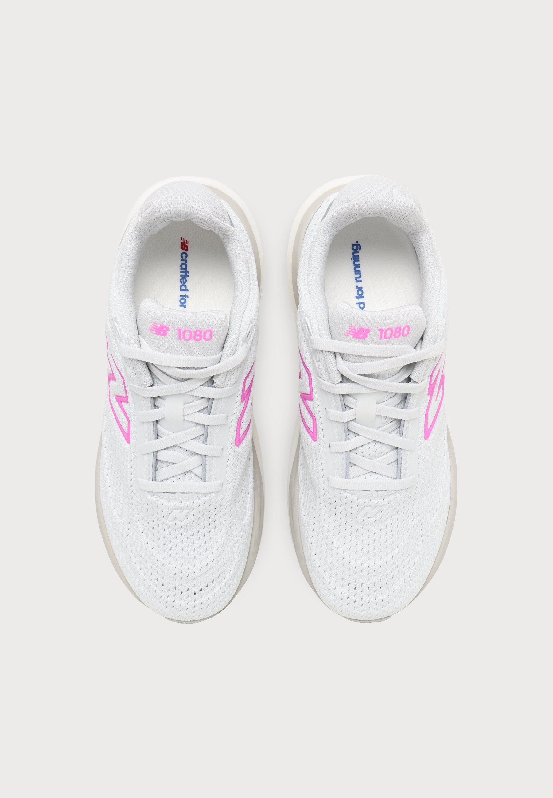 Par de zapatillas de correr New Balance 1080 blancas con logo y cordones rosas, vistas desde arriba sobre un fondo claro.