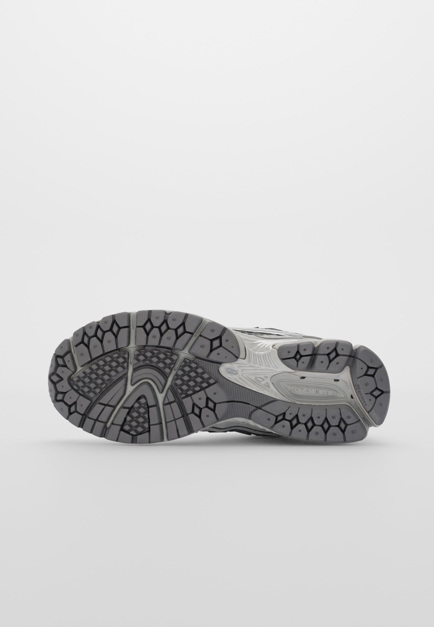Suela de zapato deportivo gris con texturas variadas, que presenta surcos profundos y multidireccionales para agarre y estabilidad. Incluye un detalle de logo.