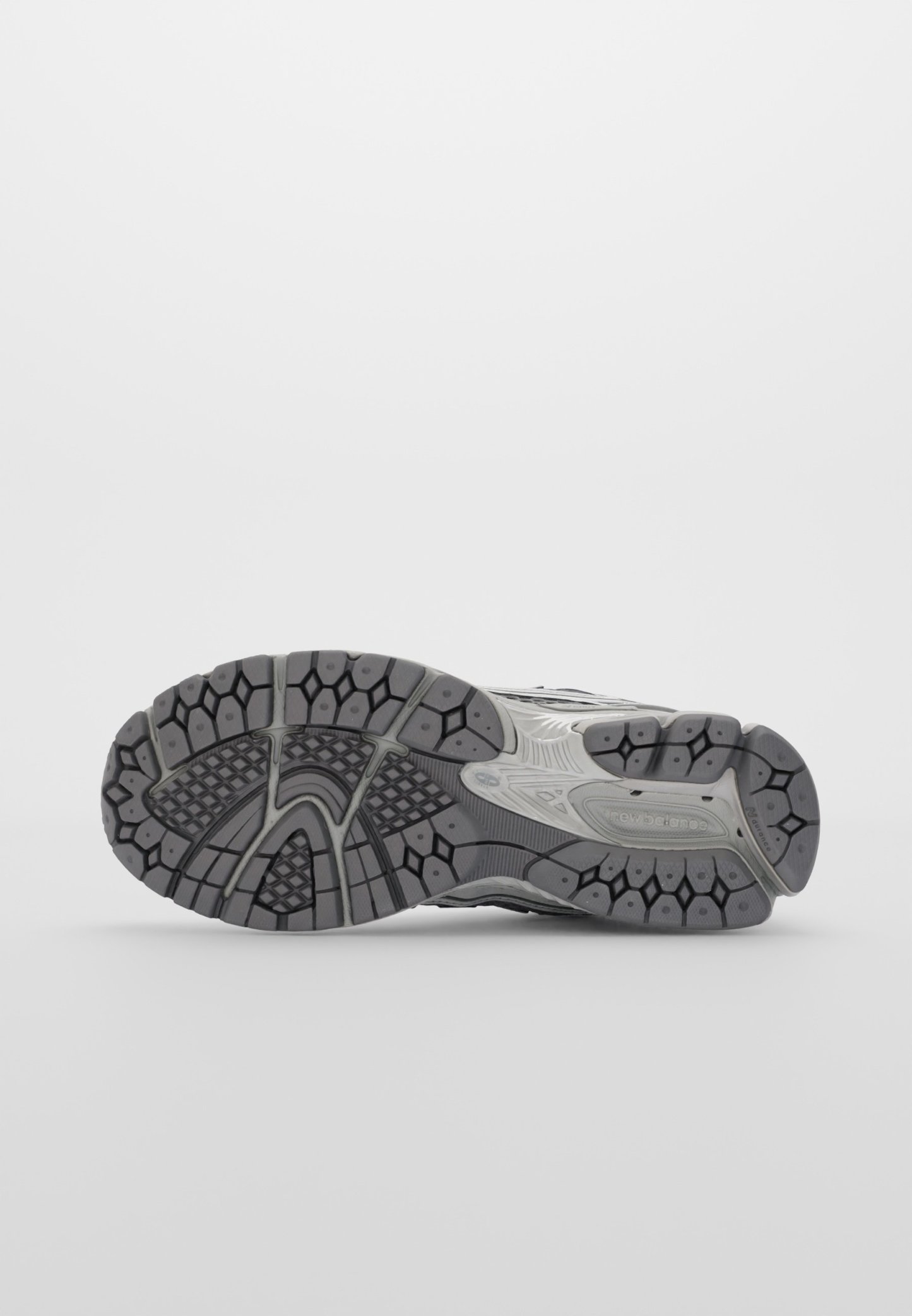 Suela de zapato deportivo gris con texturas variadas, que presenta surcos profundos y multidireccionales para agarre y estabilidad. Incluye un detalle de logo.