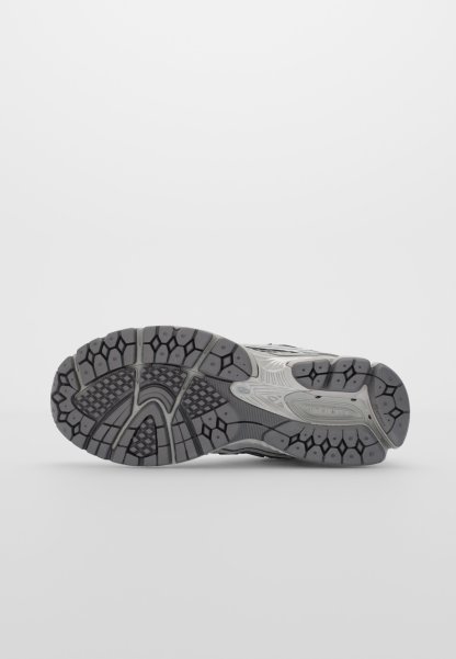 Suela de zapato deportivo gris con texturas variadas, que presenta surcos profundos y multidireccionales para agarre y estabilidad. Incluye un detalle de logo.