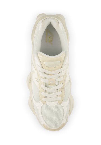 Zapatilla New Balance blanca y beige con detalles de malla y cuero, cordones atados, vista desde arriba sobre fondo blanco.