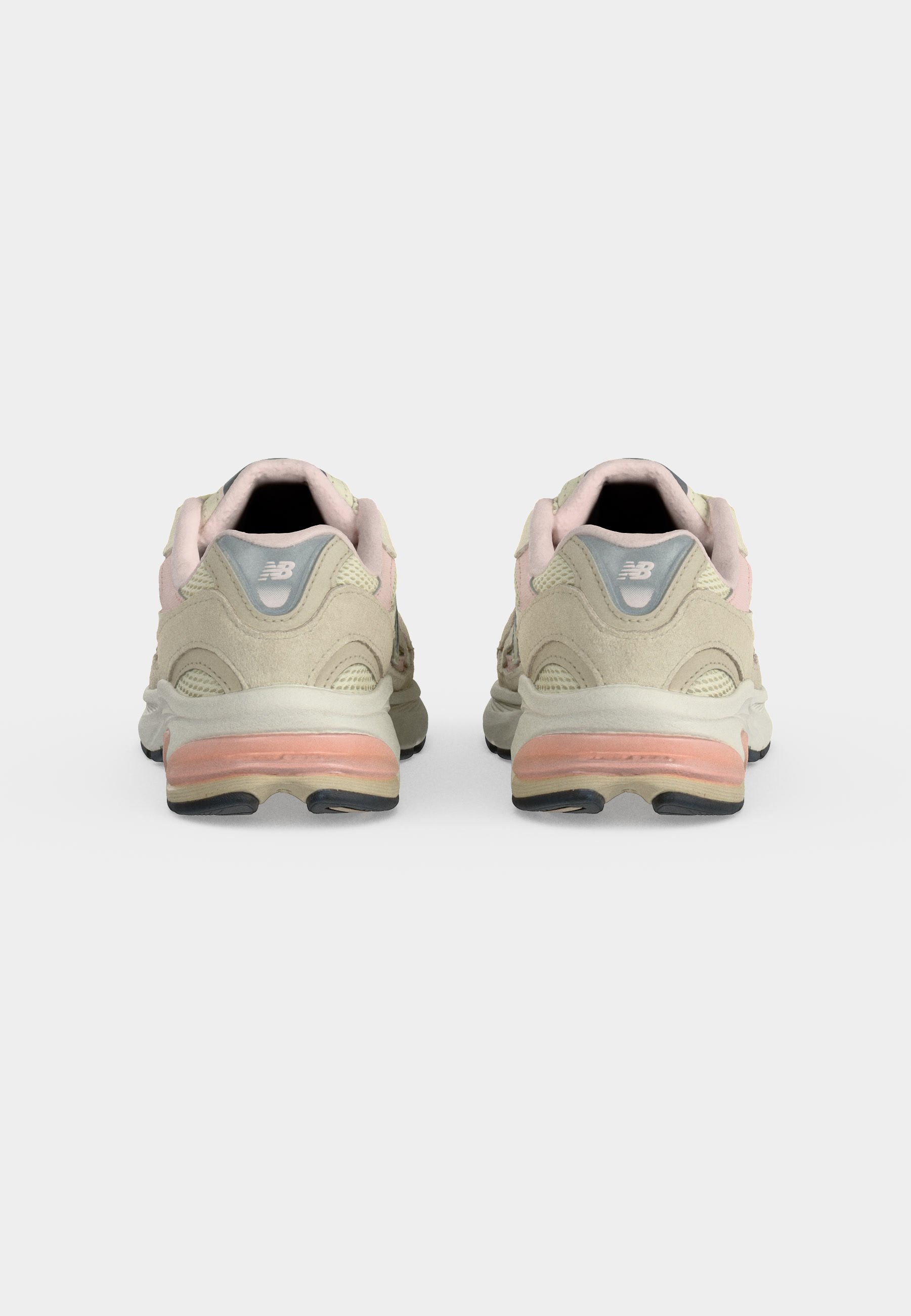 Par de zapatillas New Balance beige y rosa mostradas desde atrás con suelas acolchadas y logo en la lengüeta del talón sobre un fondo liso.