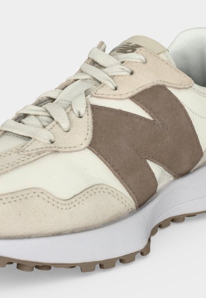 Zapatilla beige y blanca con logo "N" de ante topo, cordones blancos y suela de goma marrón claro texturizada.