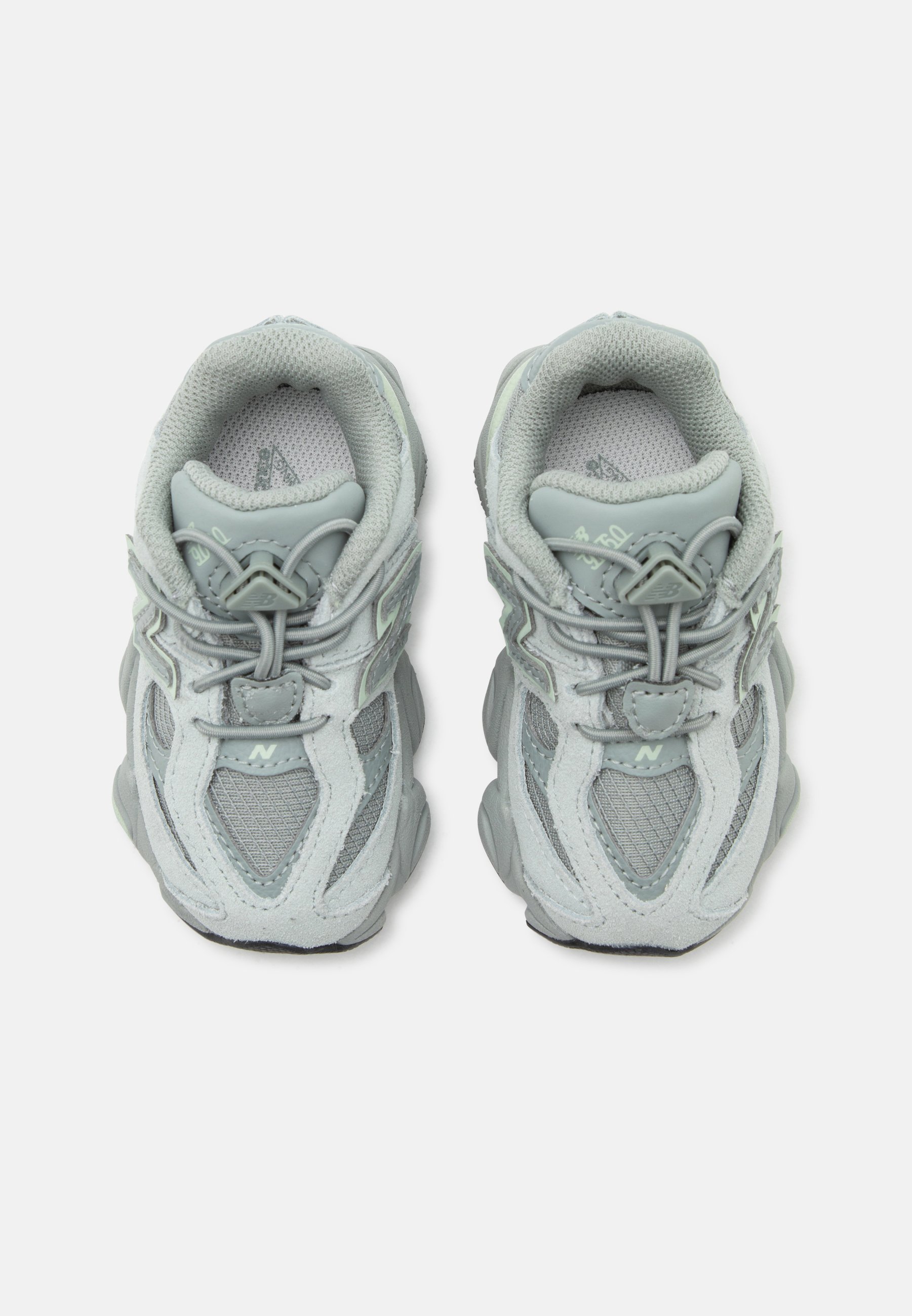 Par de zapatillas deportivas gris claro con detalles de malla y ante, cordones elásticos tipo bungee y cuello acolchado, vistas desde arriba.