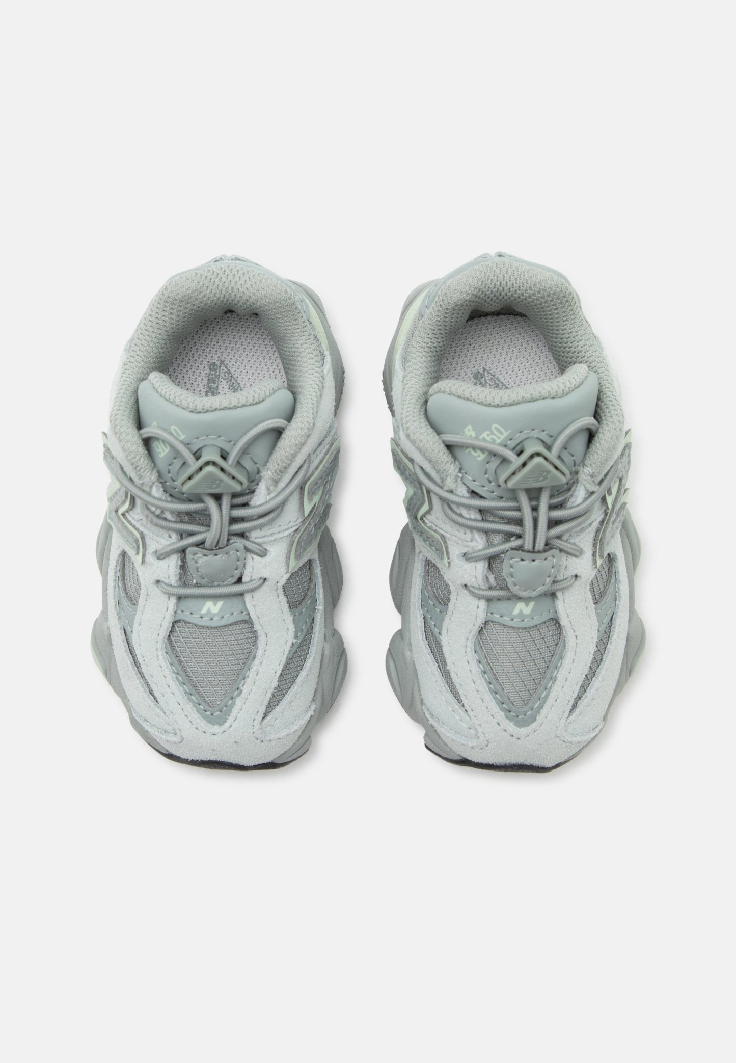 Par de zapatillas deportivas gris claro con detalles de malla y ante, cordones elásticos tipo bungee y cuello acolchado, vistas desde arriba.