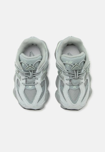 Par de zapatillas deportivas gris claro con detalles de malla y ante, cordones elásticos tipo bungee y cuello acolchado, vistas desde arriba.