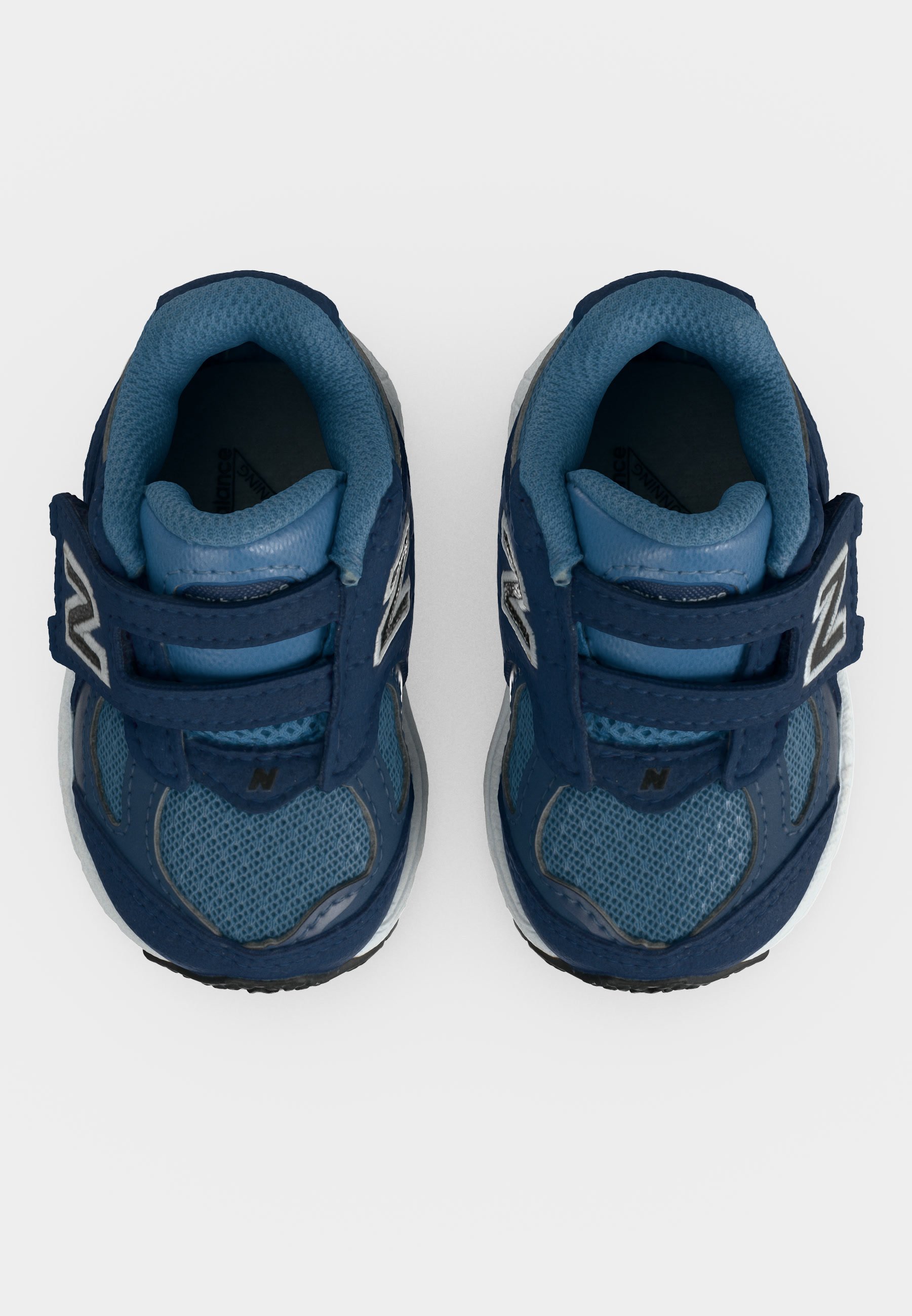 Par de zapatillas azules para niños pequeños con correas de velcro y cuellos acolchados, vistas desde arriba sobre un fondo blanco.