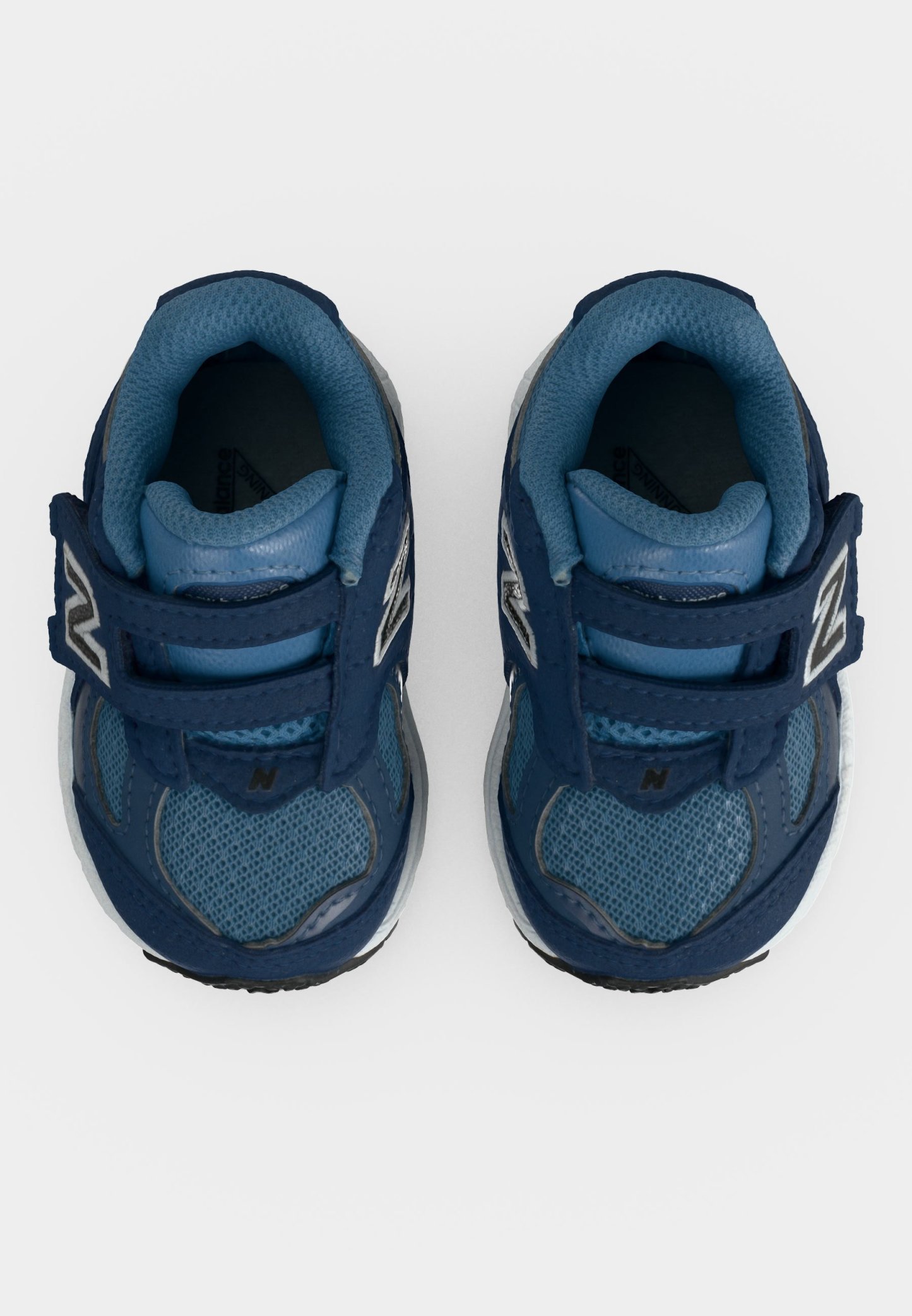 Par de zapatillas azules para niños pequeños con correas de velcro y cuellos acolchados, vistas desde arriba sobre un fondo blanco.