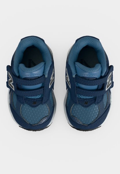 Par de zapatillas azules para niños pequeños con correas de velcro y cuellos acolchados, vistas desde arriba sobre un fondo blanco.
