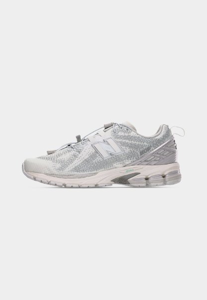 Zapatilla New Balance 1906R blanca y gris con parte superior texturizada, suela acolchada, detalles reflectantes y tira para tirar en el talón.