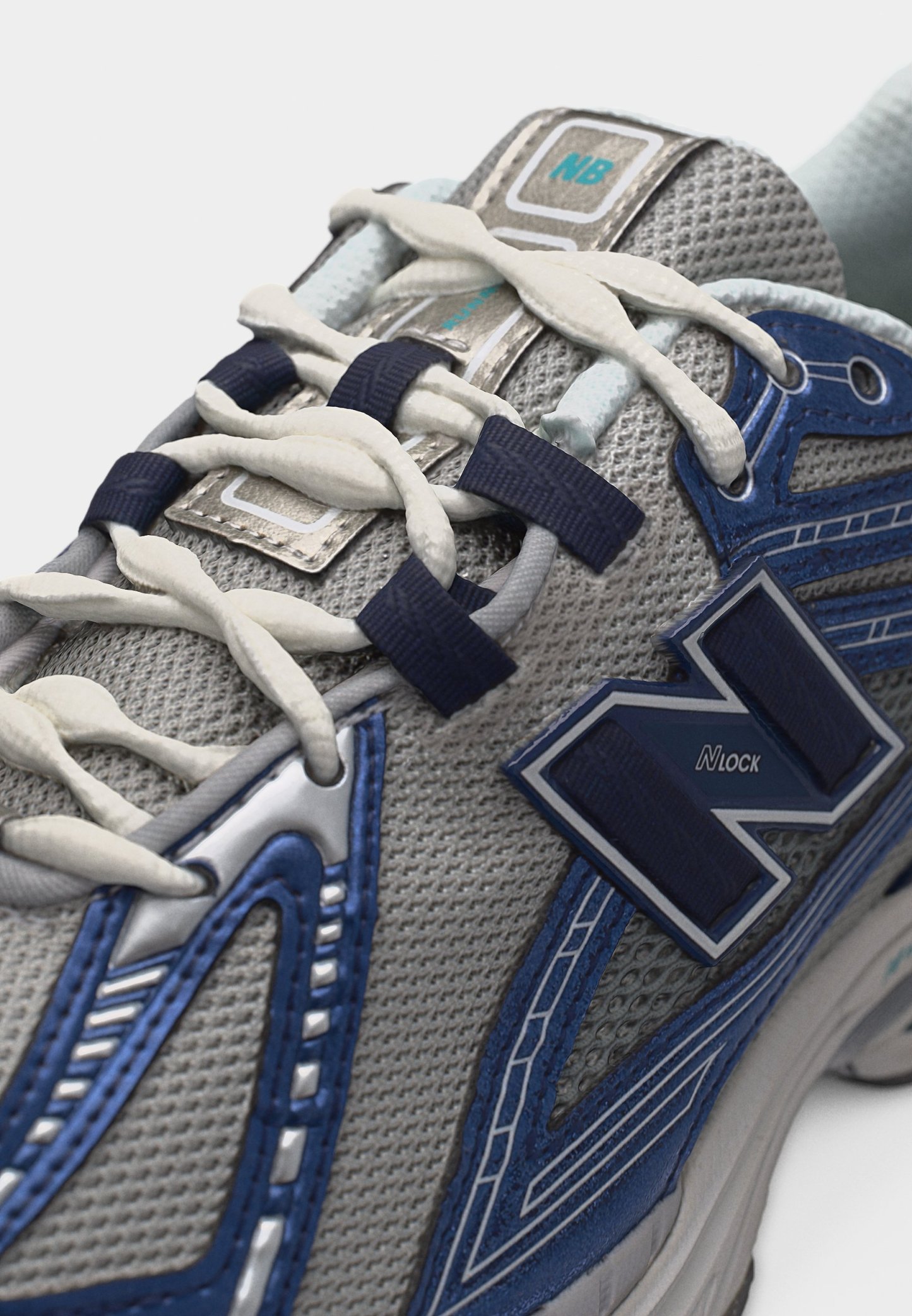 Primer plano de una zapatilla New Balance gris y azul con cordones blancos pasados por ojales azul marino y la marca "Nlock" en el lateral.