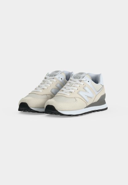 Par de zapatillas New Balance beige y grises con cordones blancos sobre un fondo liso y claro.