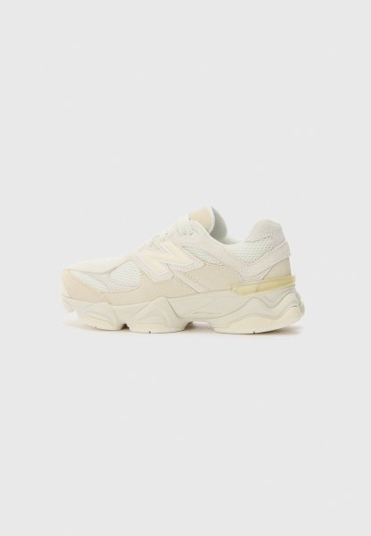 Zapatilla deportiva color crema con suela gruesa, paneles de malla y ante, cierre con cordones y logo "N" en el lateral, mostrada sobre un fondo claro y sencillo.